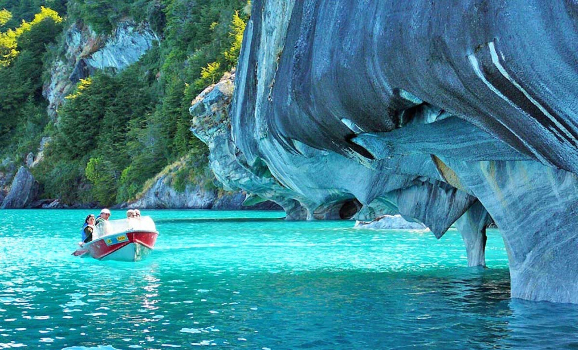 A boat near a large rock formation in clear turquoise water.
