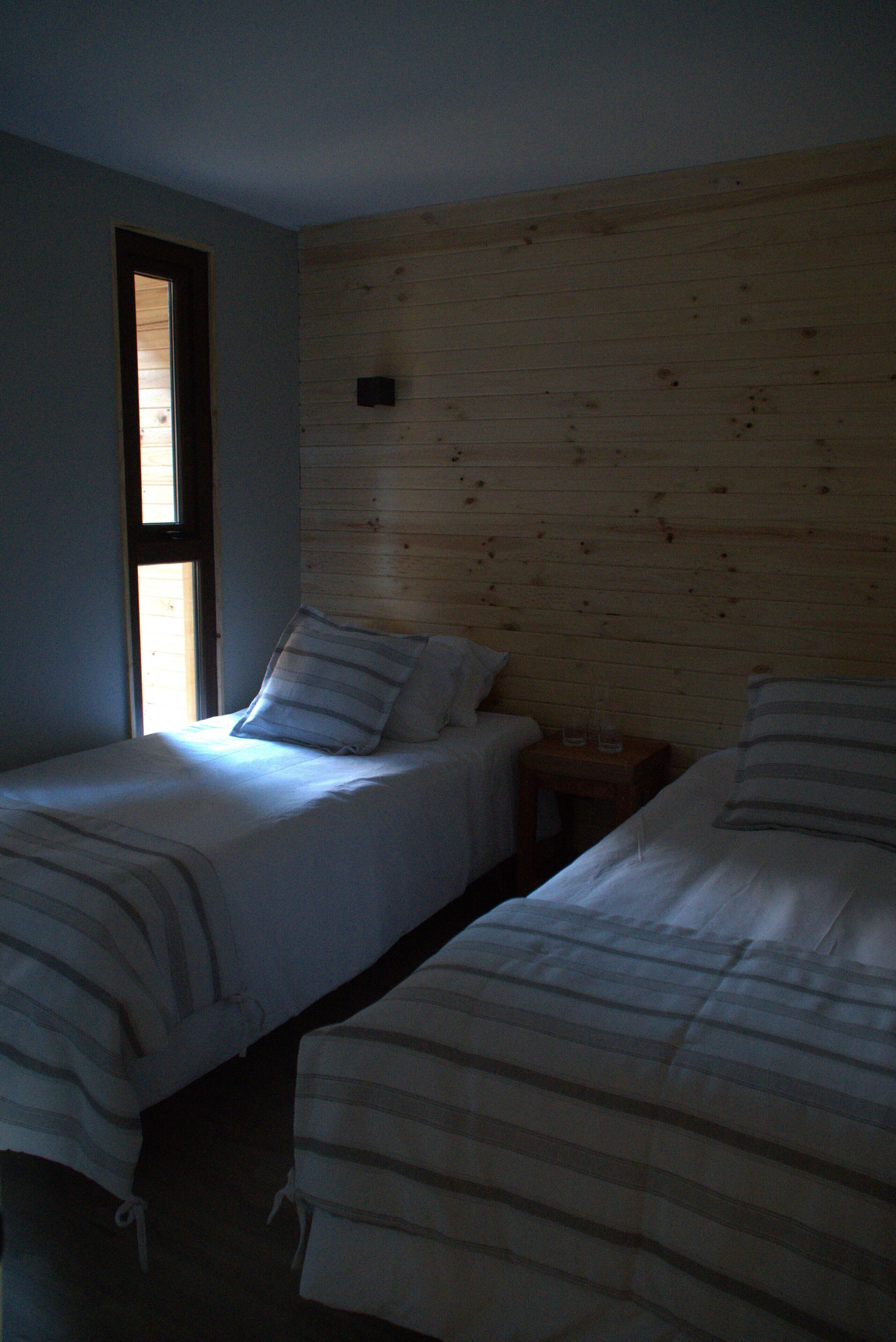 A room with two beds, each with striped bedding, a small wooden nightstand, and a window with blinds.