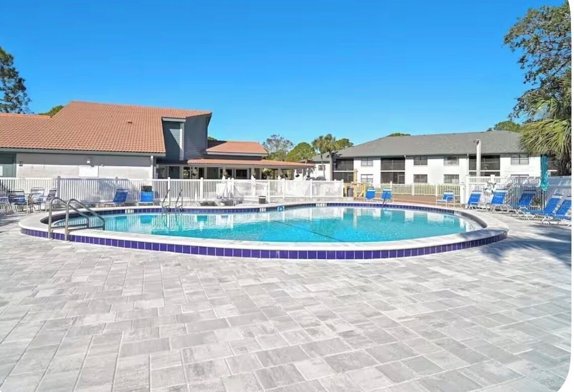 A swimming pool with a tiled deck, surrounded by lounge chairs and a white fence.