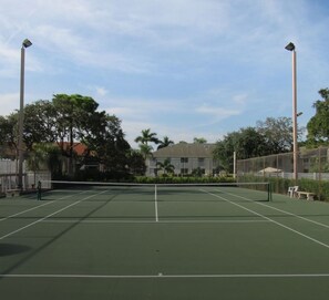 A tennis court with a net, surrounded by trees and a building in the background.