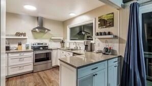 A modern kitchen with white and light blue cabinets, stainless steel appliances, and a large window above the sink.