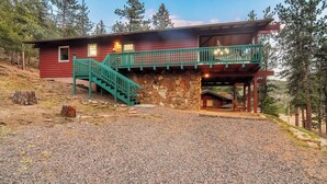A two-story log cabin with a stone foundation, a green staircase, and a porch with a railing.