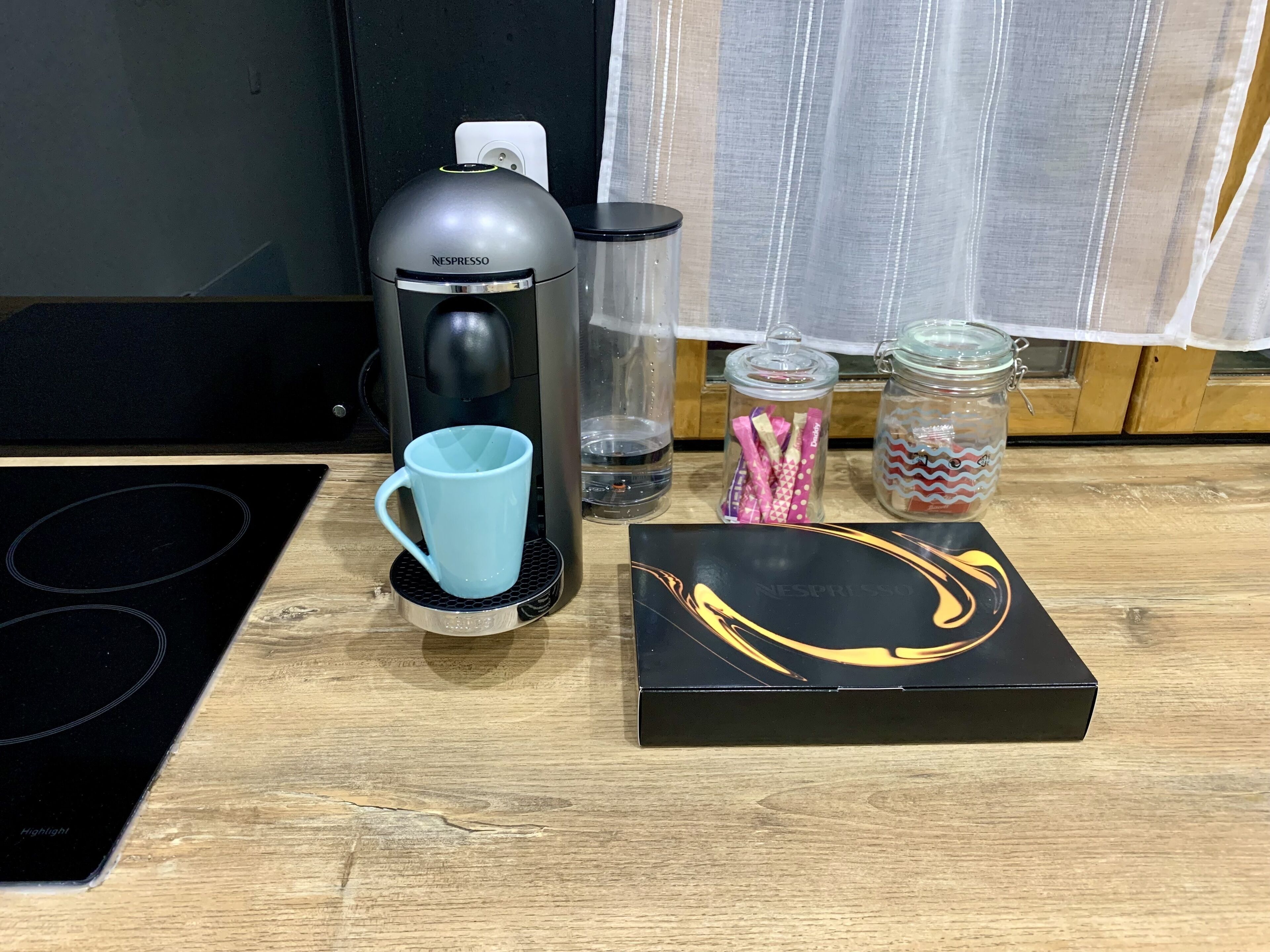Une cuisine équipée d’une machine à café Nespresso, d’une tasse bleue, d’un bocal en verre rempli de bonbons et d’une boîte.