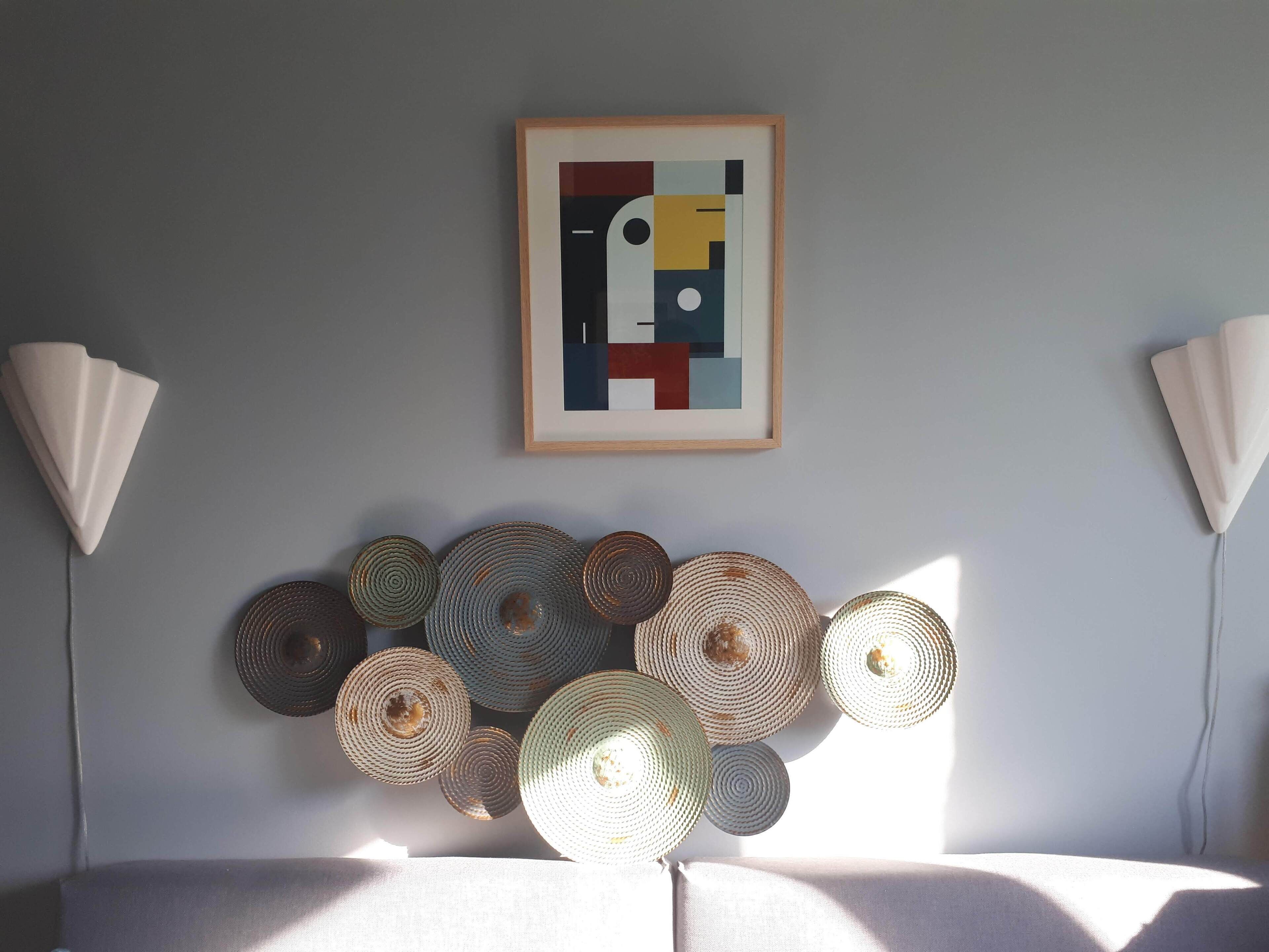 Une pièce décorée d’un tableau abstrait encadré, d’une série de luminaires tressés et de deux lampes fixées au mur.