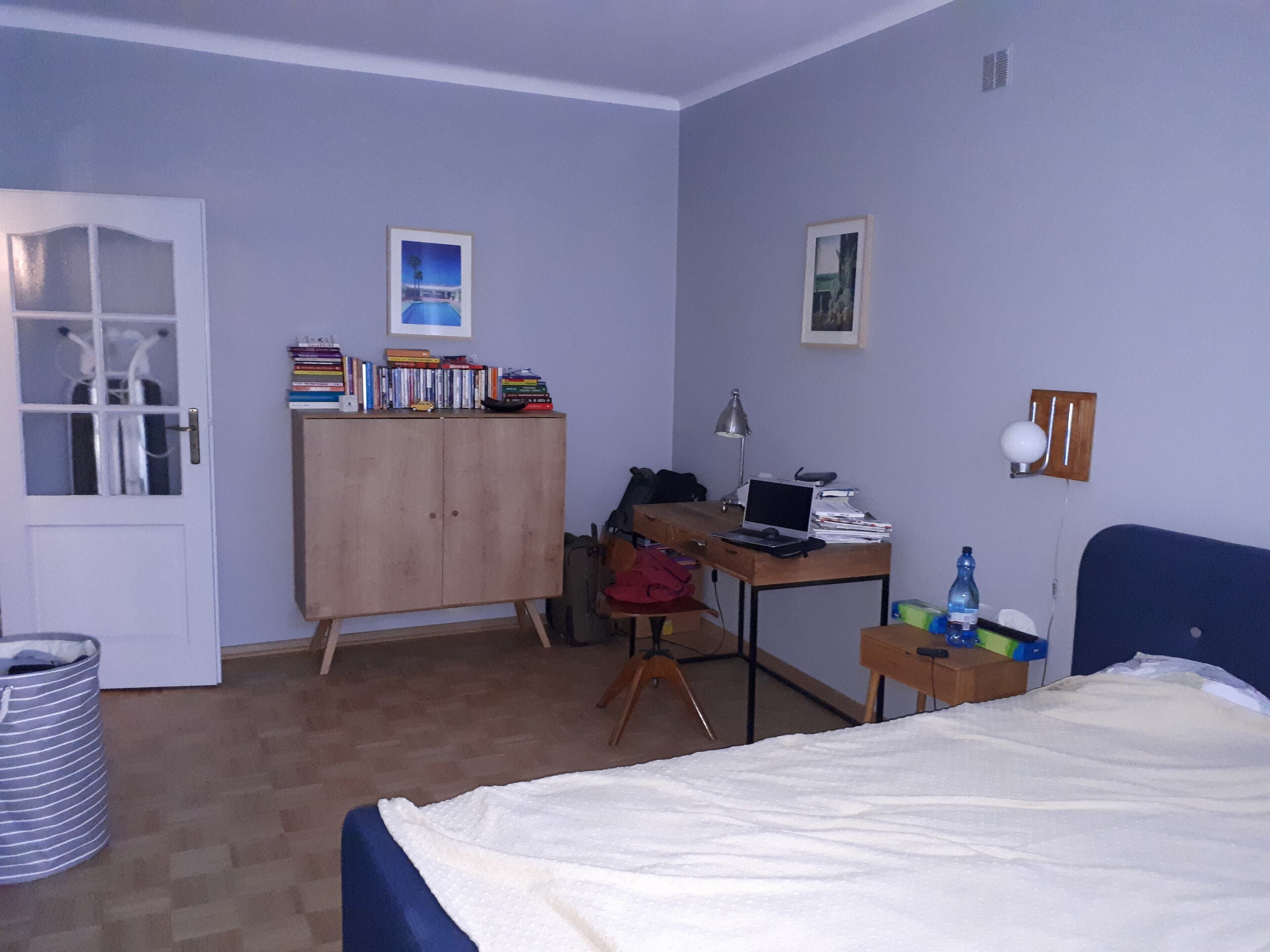A bedroom with a bed, a desk with a laptop, a wardrobe, and a door with a window.