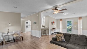 A spacious living room with a gray couch, a coffee table, and a dining area with a white table and chairs. - Sand Dollars - 5mins to beach, huge lot, pet friendly and boat parking!  (Ocean Isle Beach)