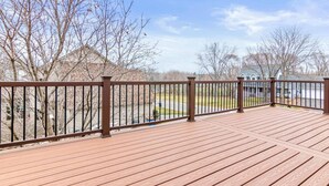 A wooden deck with a brown metal railing, overlooking a residential area with houses and leafless trees.