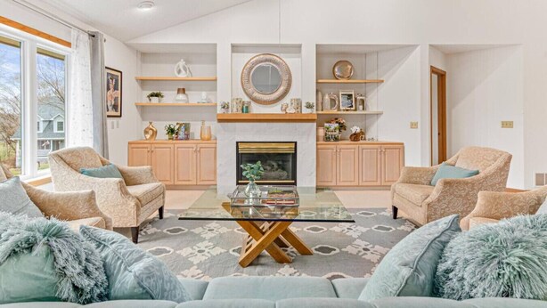 A spacious living room with two sofas, a coffee table, and a fireplace. There are shelves with decorative items and a large mirror above the fireplace.