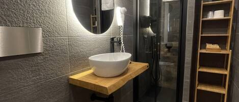A modern bathroom with a large oval mirror, a white sink, and a glass-enclosed shower.