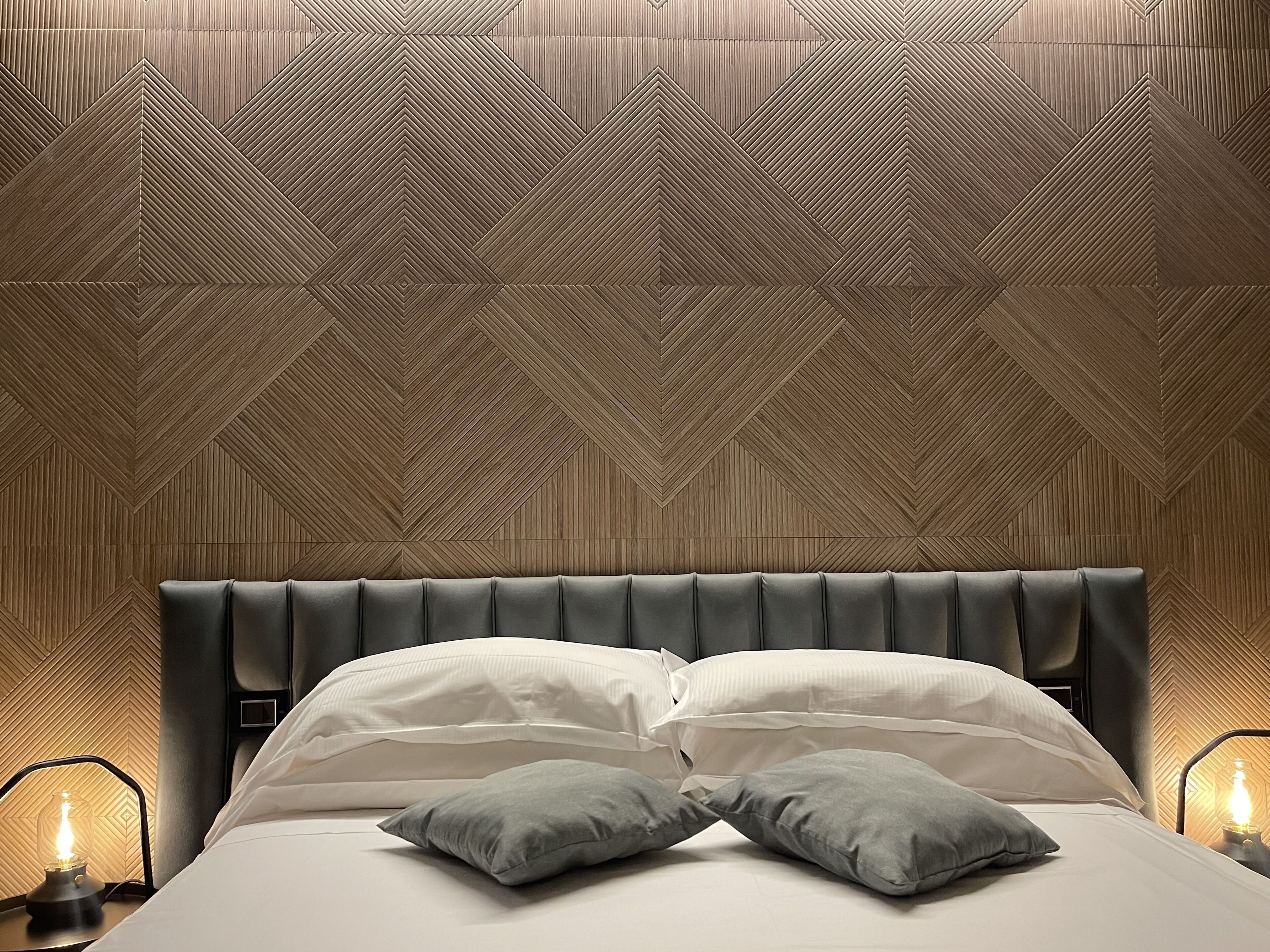 A neatly made bed with a headboard, two pillows, and bedside lamps.