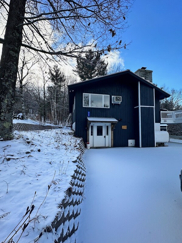 A dark blue building with a white door and windows, surrounded by snow-covered ground and trees. - Nature’s Nest located in the heart of Wilmington, 5 minutes from Whiteface Mt.! (Wilmington)