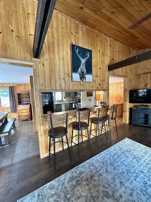 A rustic wooden interior with a bar area, wooden ceiling beams, and a large deer painting. - Nature’s Nest located in the heart of Wilmington, 5 minutes from Whiteface Mt.! (Wilmington)