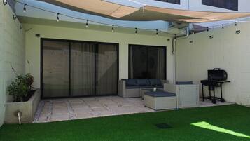 A patio area with a seating arrangement, a barbecue grill, and a covered space with string lights.