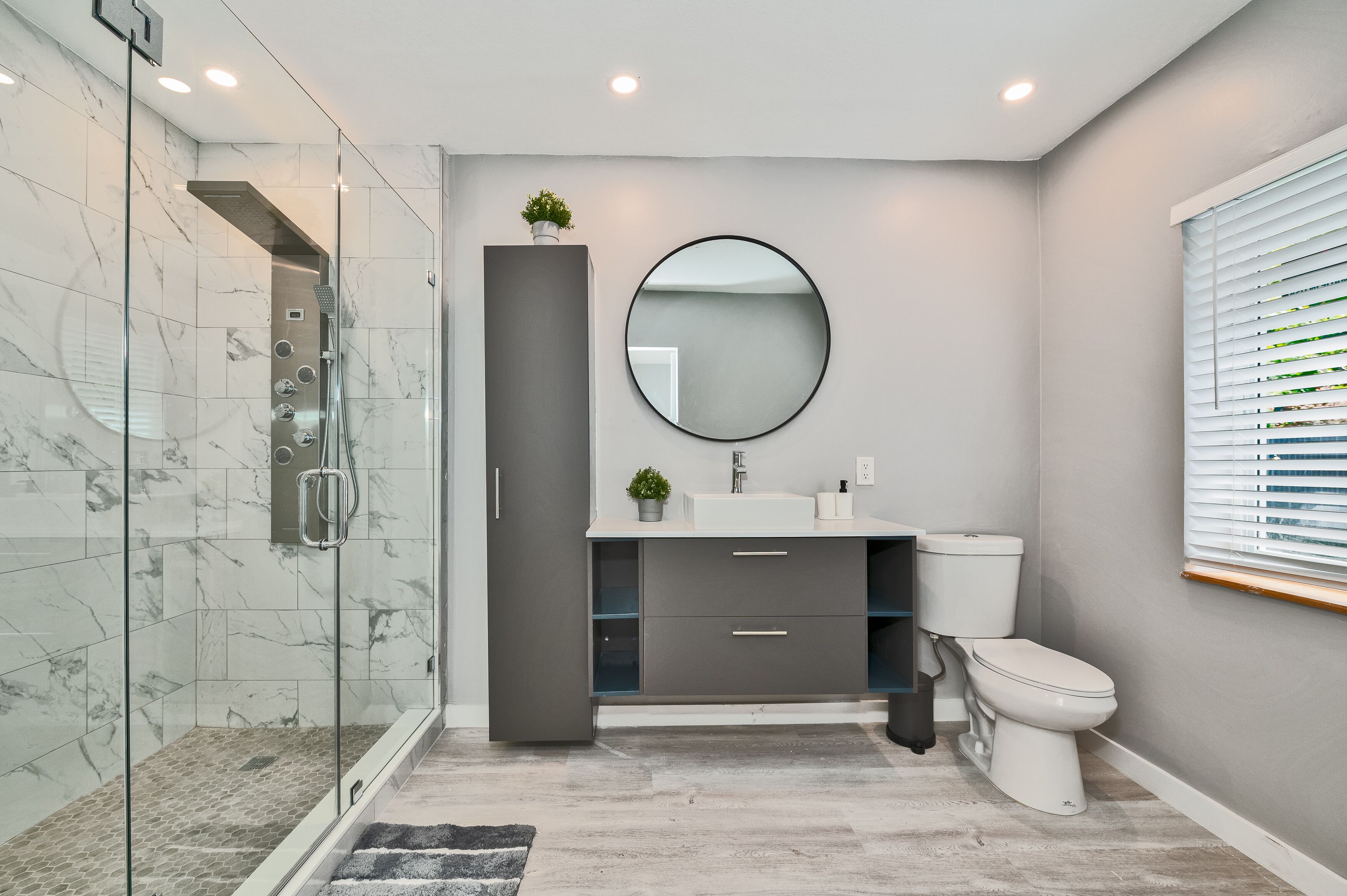 A modern bathroom with a glass-enclosed shower, a grey vanity with a mirror, and a toilet.