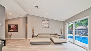 A spacious living room with a large sectional sofa, a painting, and a view of a swimming pool. - Spacious 4 bedrooms, 2 bathroom house with pool (Miramar)