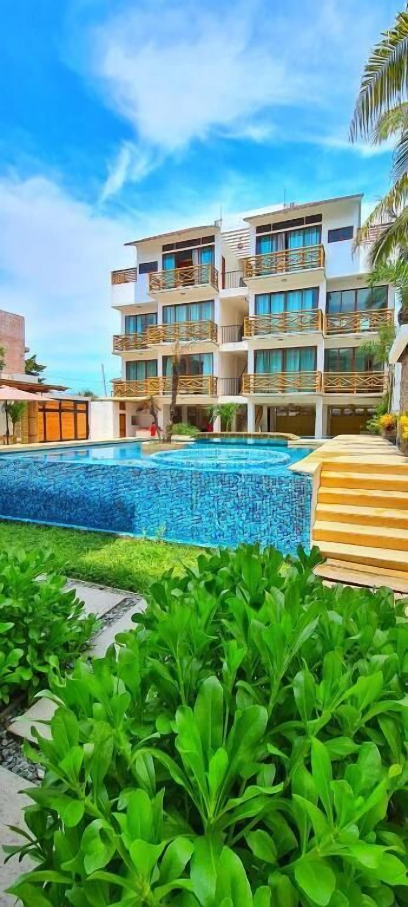 Et hotel med flere etager og en swimmingpool omgivet af frodig vegetation.