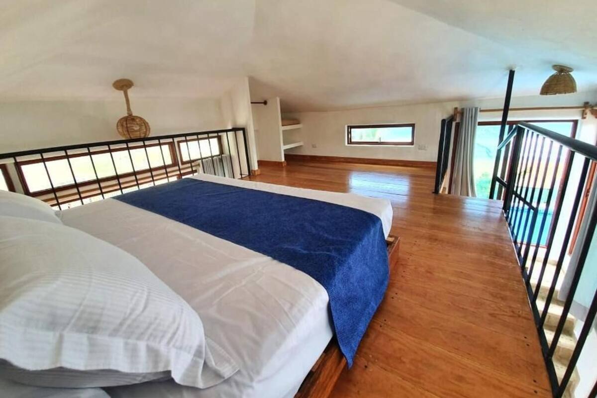 Amplia habitación con una cama grande, piso de madera, balcón con barandilla y ventana que proporciona luz natural.