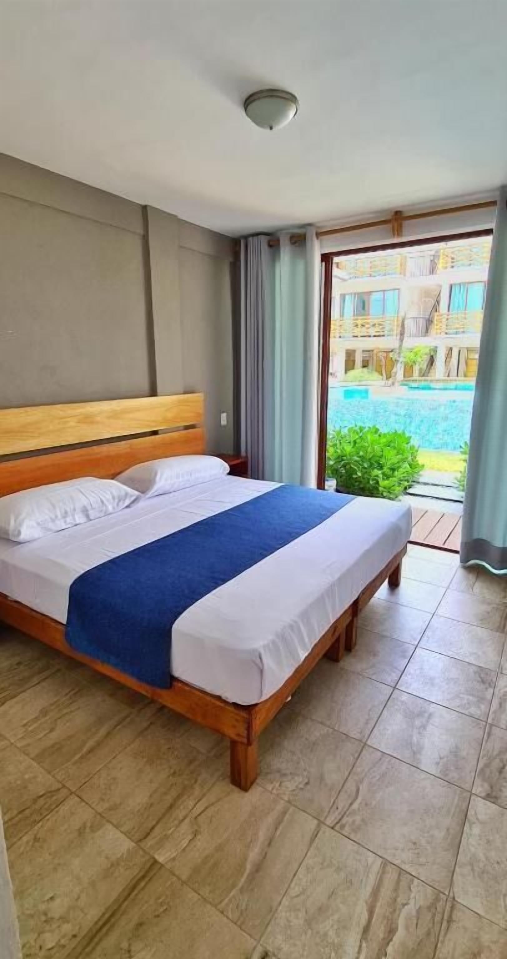 A hotel room with a bed, a view of a swimming pool, and a balcony with curtains.