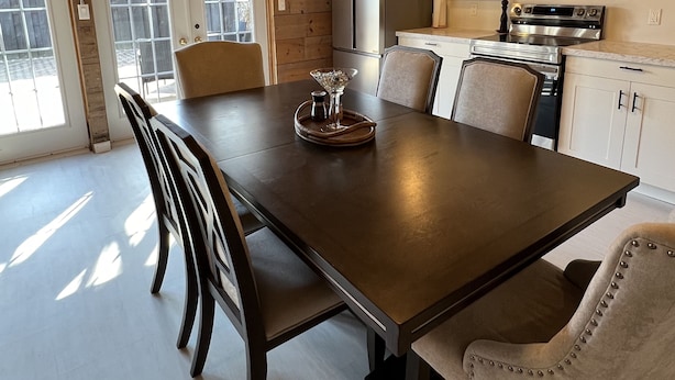 A modern kitchen with a large dining table, white cabinets, and stainless steel appliances. - Vintage Roost at Fleming Farms (Lincoln)