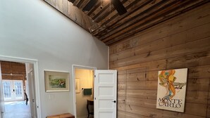 A bedroom with a wooden ceiling, a bed with a floral bedspread, a bench, and a door leading to another room. - Vintage Roost at Fleming Farms (Lincoln)