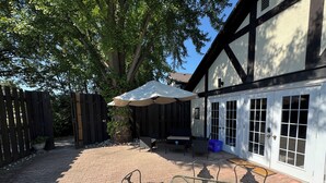 A patio area with a table and chairs, a covered seating area, and a building with a black and white facade. - Vintage Roost at Fleming Farms (Lincoln)