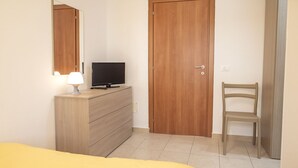Un dormitorio con una cama, un tocador, un televisor, una puerta de madera y una silla.