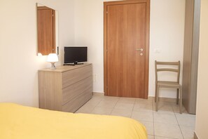 Un dormitorio con una cama, un tocador, un televisor, una puerta de madera y una silla.