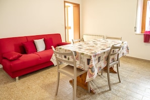 A room with a red sofa, a table with a patterned tablecloth, and a window with a view.