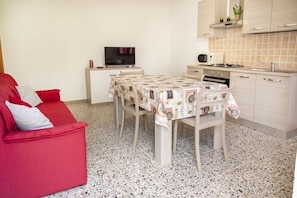Un espacio habitable compacto con un sofá rojo, una mesa de comedor con mantel estampado, un televisor sobre un mueble, un microondas y un salpicadero de cocina con azulejos.