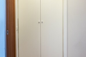 Une armoire blanche fermée, dotée de deux poignées, d’un cadre de porte en bois et placée devant un mur blanc.