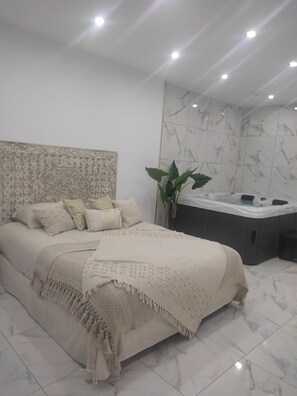 A modern bedroom with a large bed, a decorative headboard, a jacuzzi, and a potted plant.