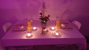 A table set for two with a candle centerpiece, two drinks, and a vase with flowers. - Studio Romantique Indépendant Avec Jacuzzi (Saint-Andiol)