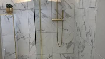 Una ducha moderna con puerta de vidrio, azulejos de mármol y cabezal de ducha dorado.