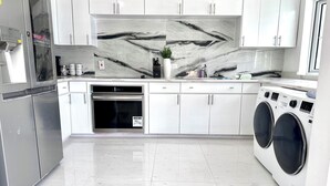 Une cuisine moderne avec des meubles blancs, un réfrigérateur en acier inoxydable, un four et un lave-linge.
