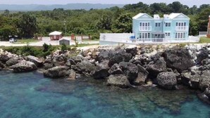 Une propriété située sur la côte, avec une grande maison, une eau d’un bleu limpide et un rivage rocheux.