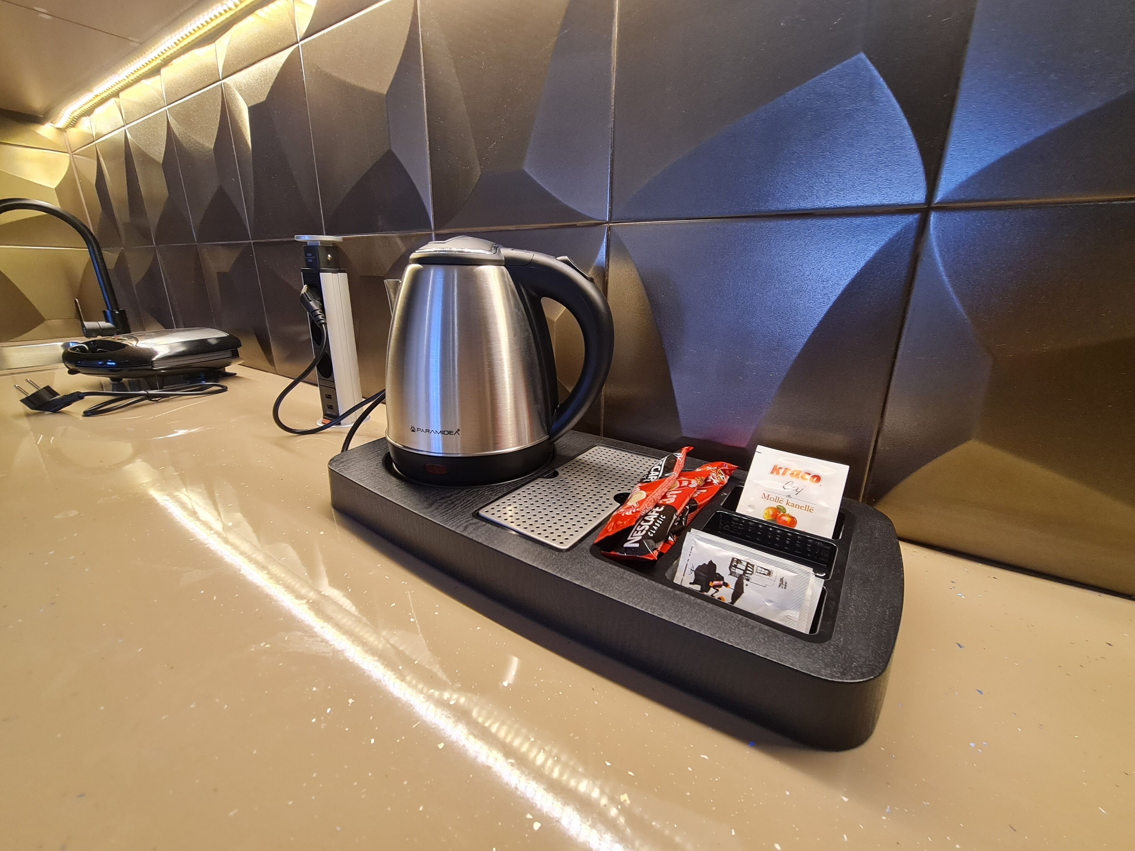 Un mini-bar d’hôtel comprenant une bouilloire, une multiprise et un assortiment de collations.