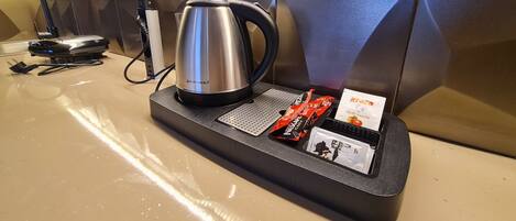 A hotel minibar setup with a kettle, a power strip, and a snack package.
