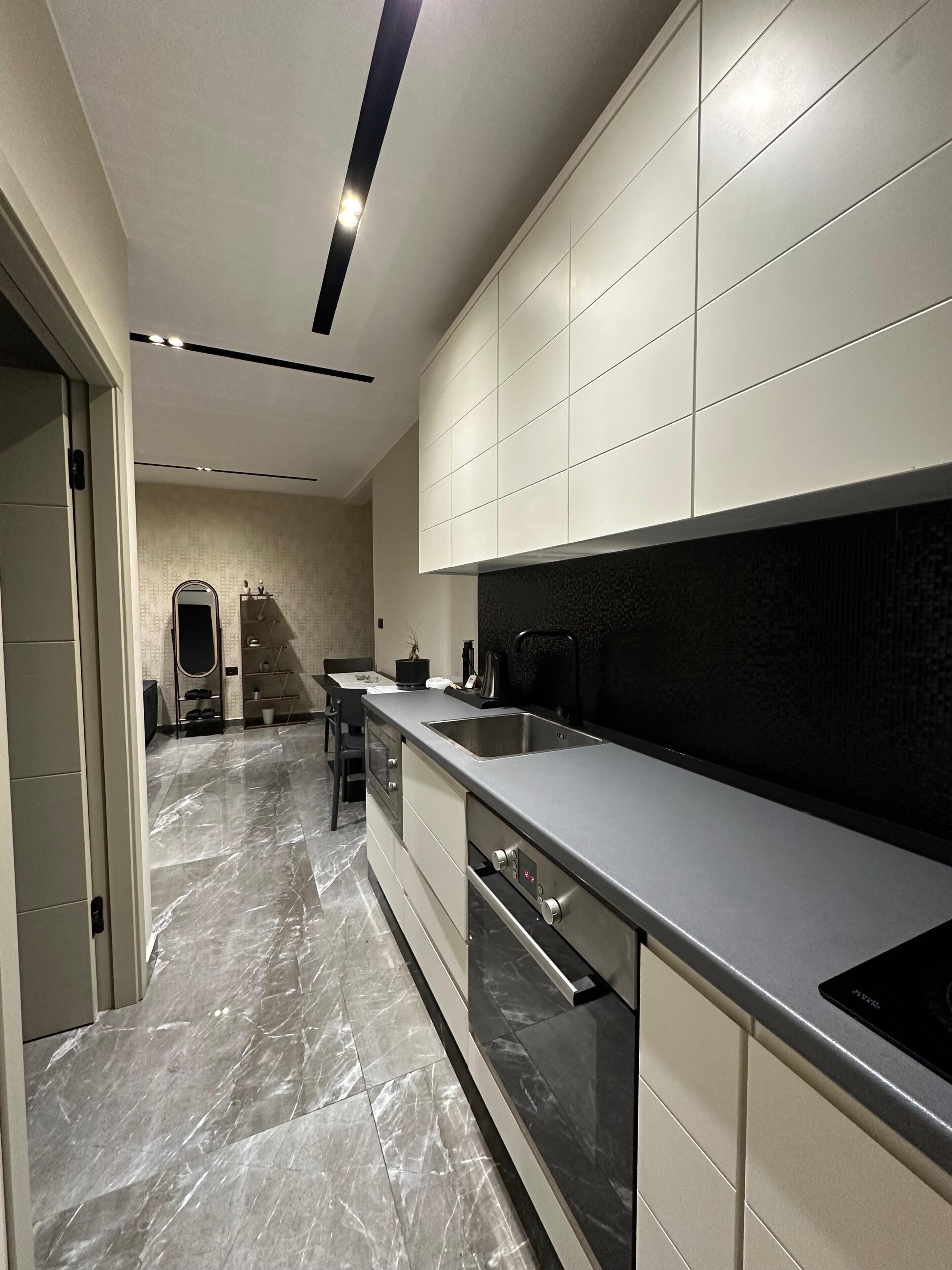 A modern kitchen with a marble floor, stainless steel appliances, and a black backsplash.