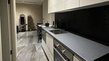A modern kitchen with a marble floor, stainless steel appliances, and a black backsplash.