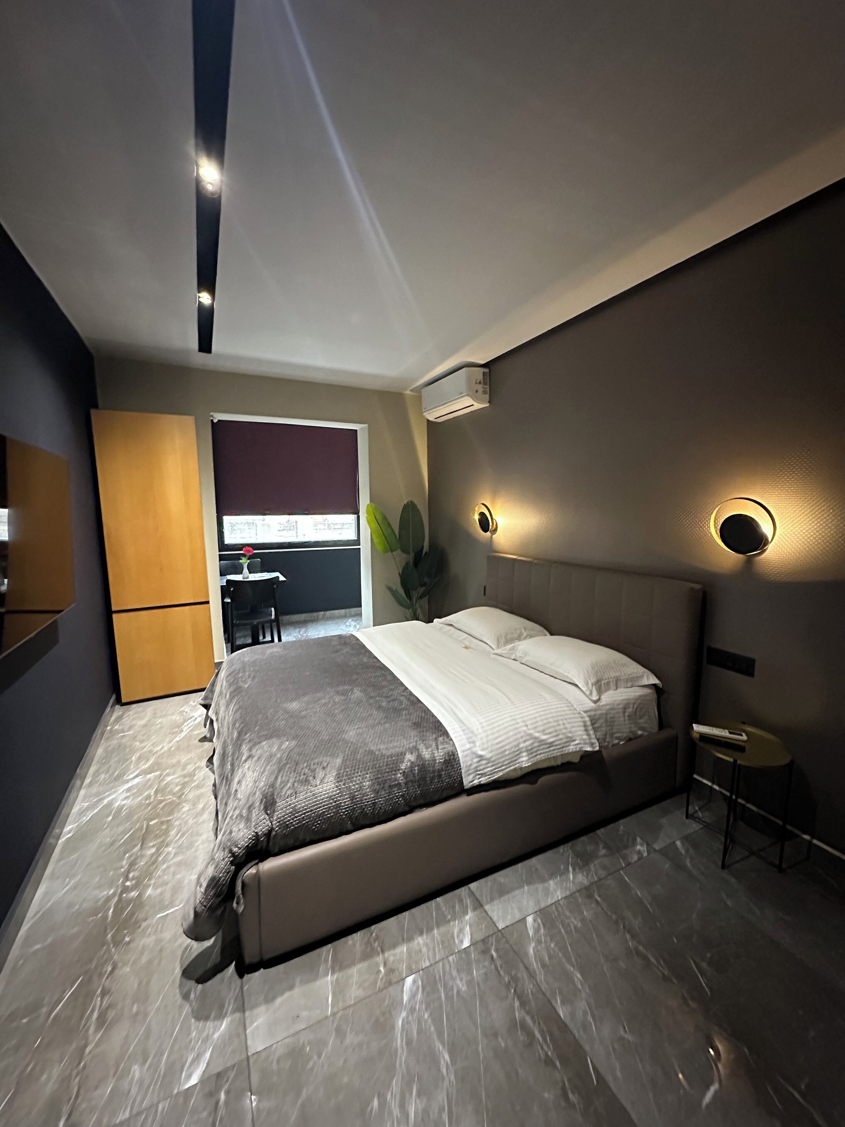 A modern bedroom with a bed, a small table, and a potted plant.