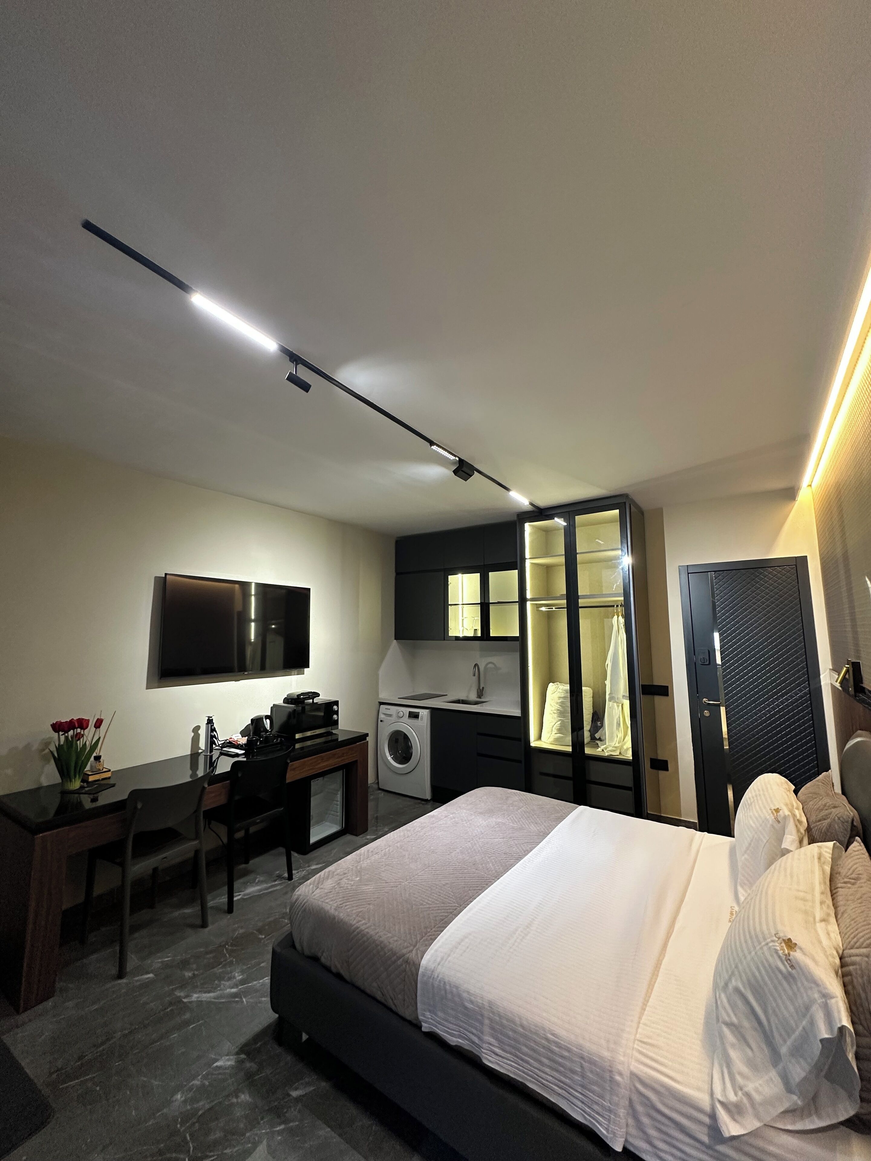 A modern bedroom with a bed, desk, and built-in washer-dryer.