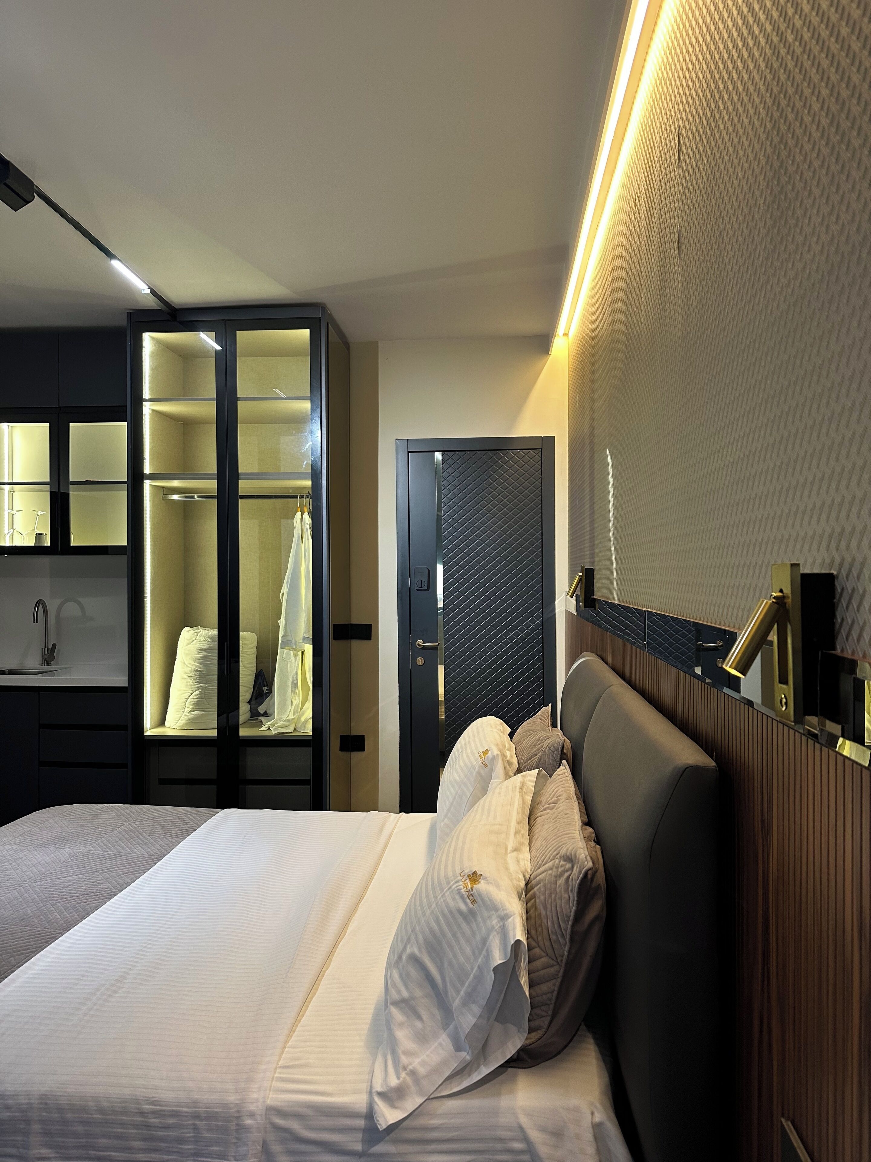 Een moderne hotelkamer met een groot bed, een inloopkast, een badkamer met spiegel en een nachtkastje.