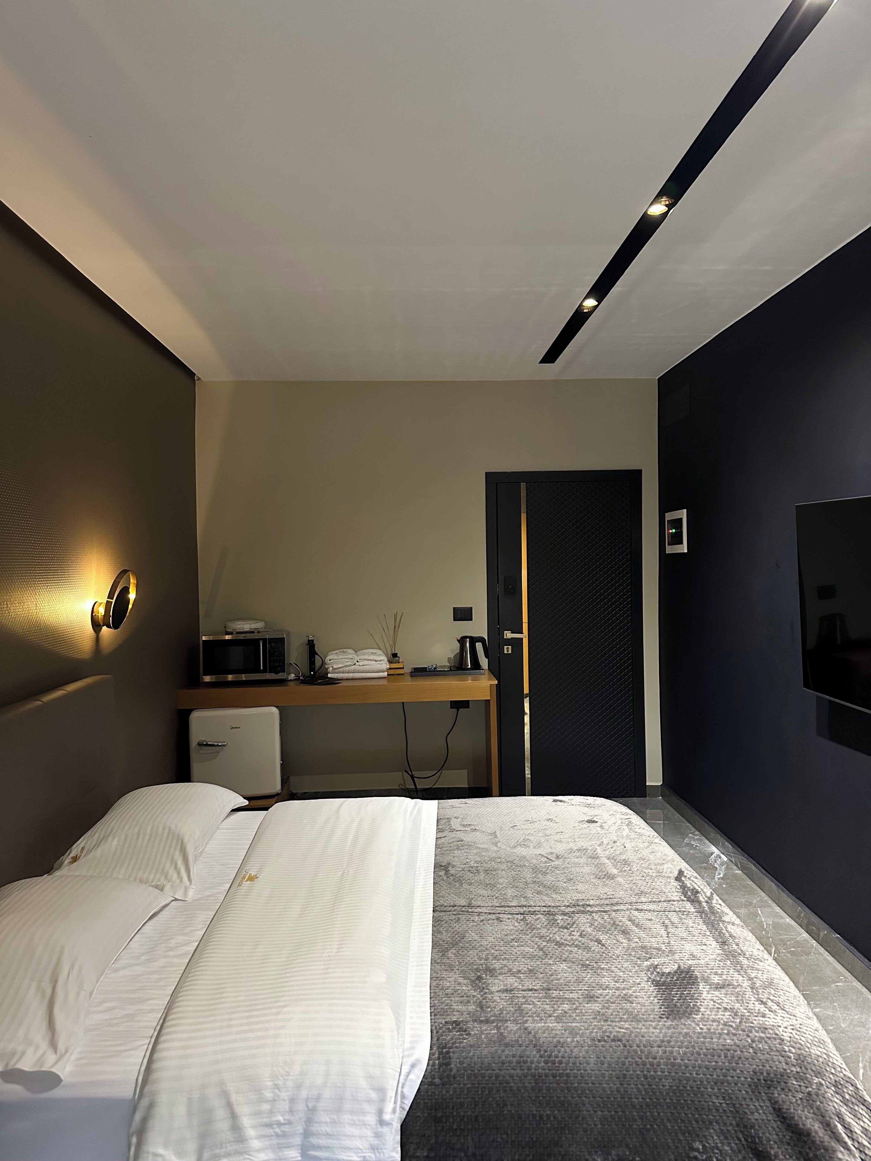 A modern bedroom with a bed, a desk, a microwave, and a small refrigerator.