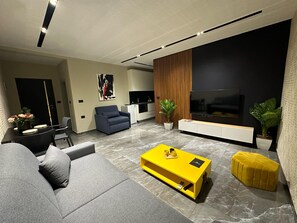 A modern living room with a sofa, a yellow coffee table, a TV, and a kitchen area in the background.