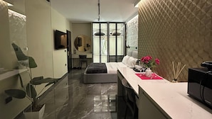 Una habitación de hotel moderna con separador de vidrio, una cama, un escritorio con computadora y una zona de cocina.