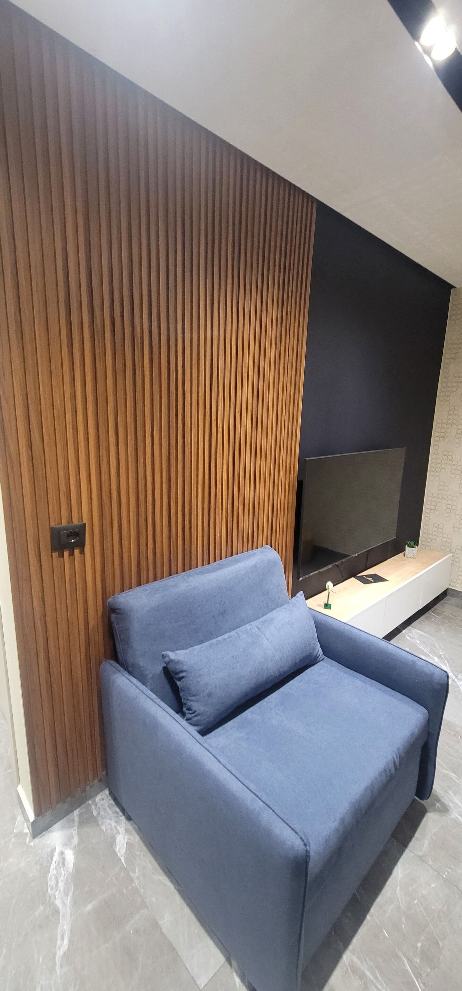 A modern living room with a blue sofa, a wooden slatted wall, and a flat-screen TV on a wooden console.