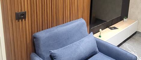 A modern living room with a blue sofa, a wooden slatted wall, and a flat-screen TV on a wooden console.