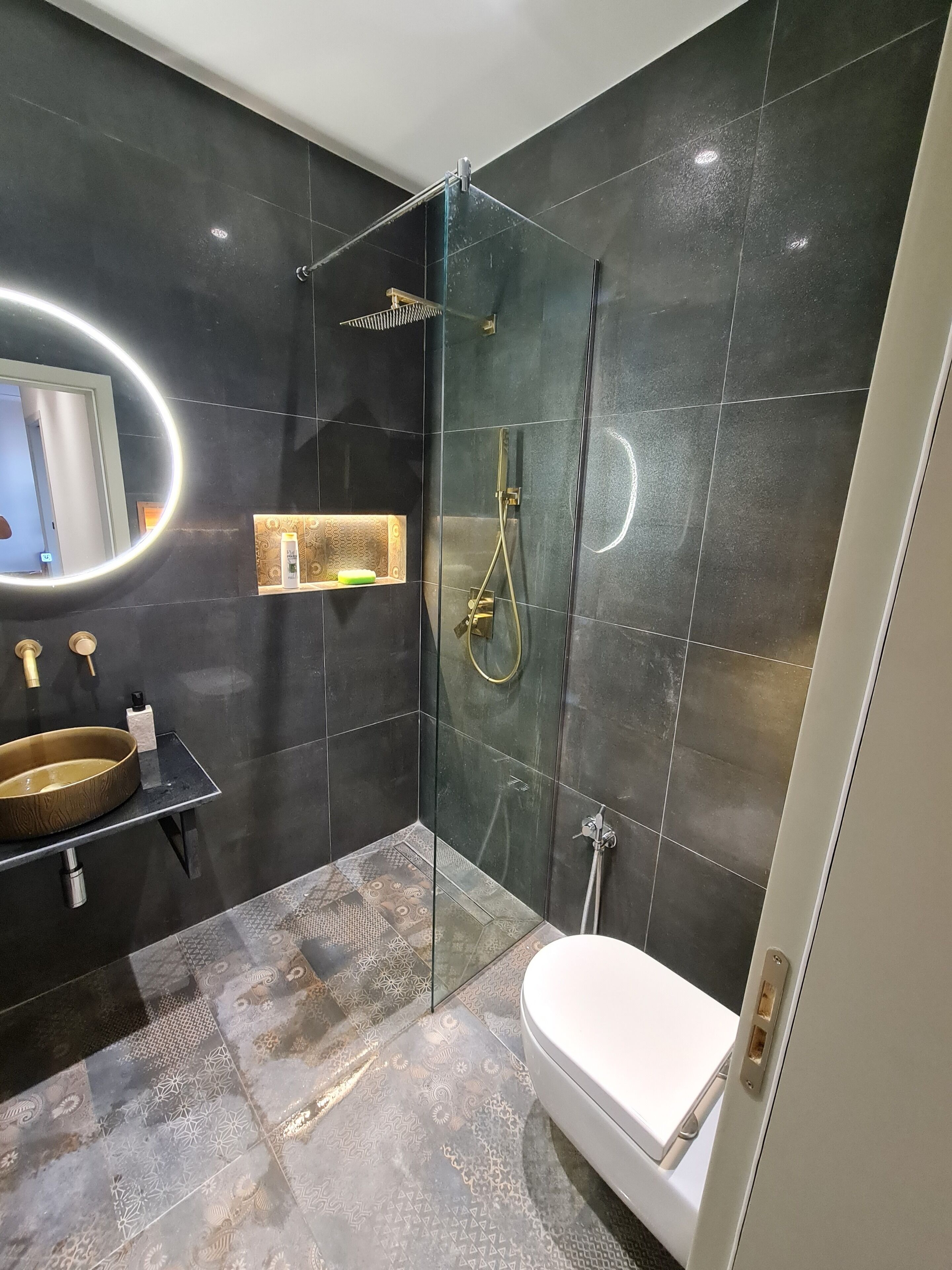 A modern bathroom with a glass-enclosed shower, a white toilet, and a vanity with a gold sink.
