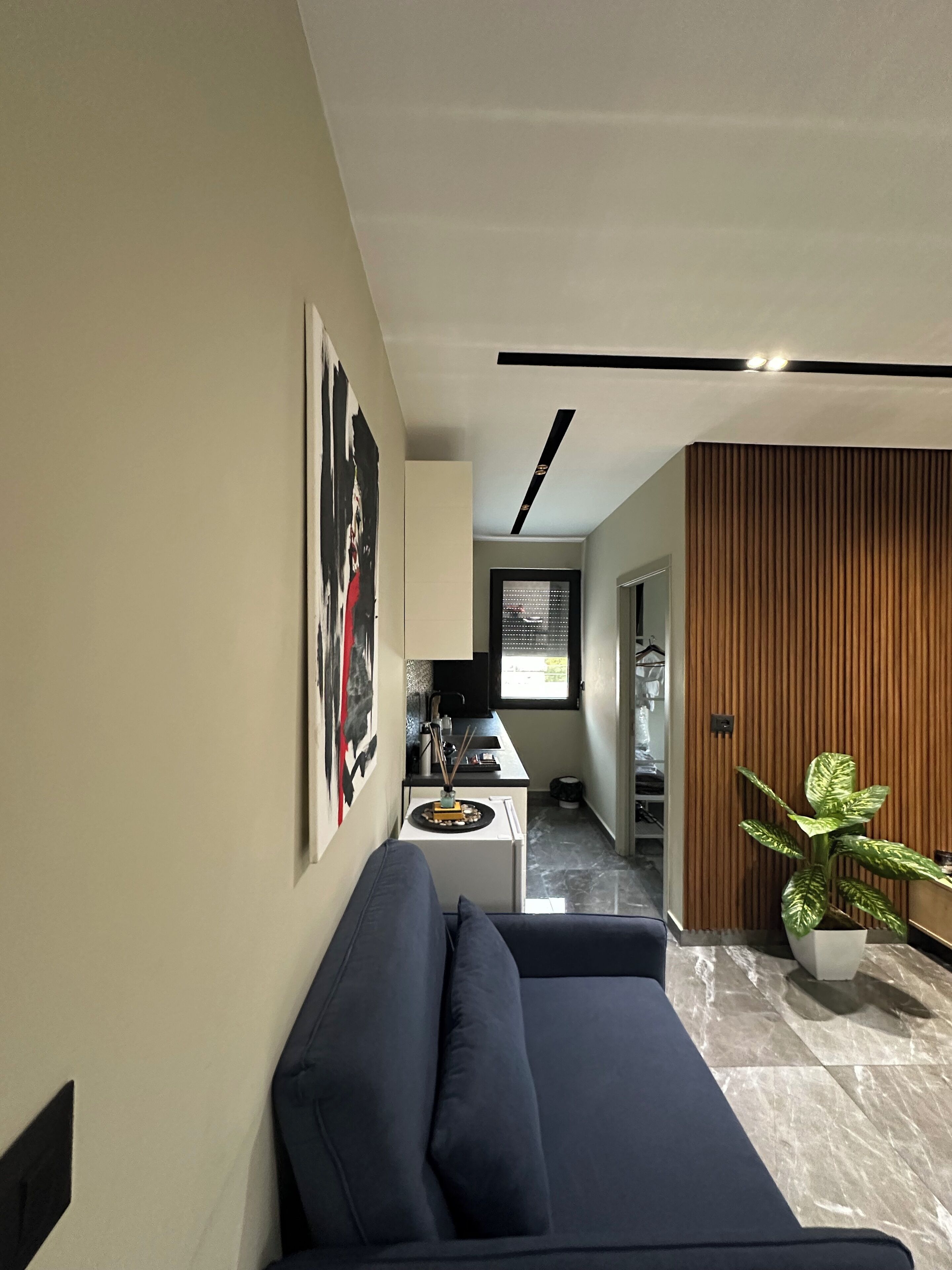 Una sala moderna con un sofá de color oscuro, una cocina al fondo y un panel de pared de madera.