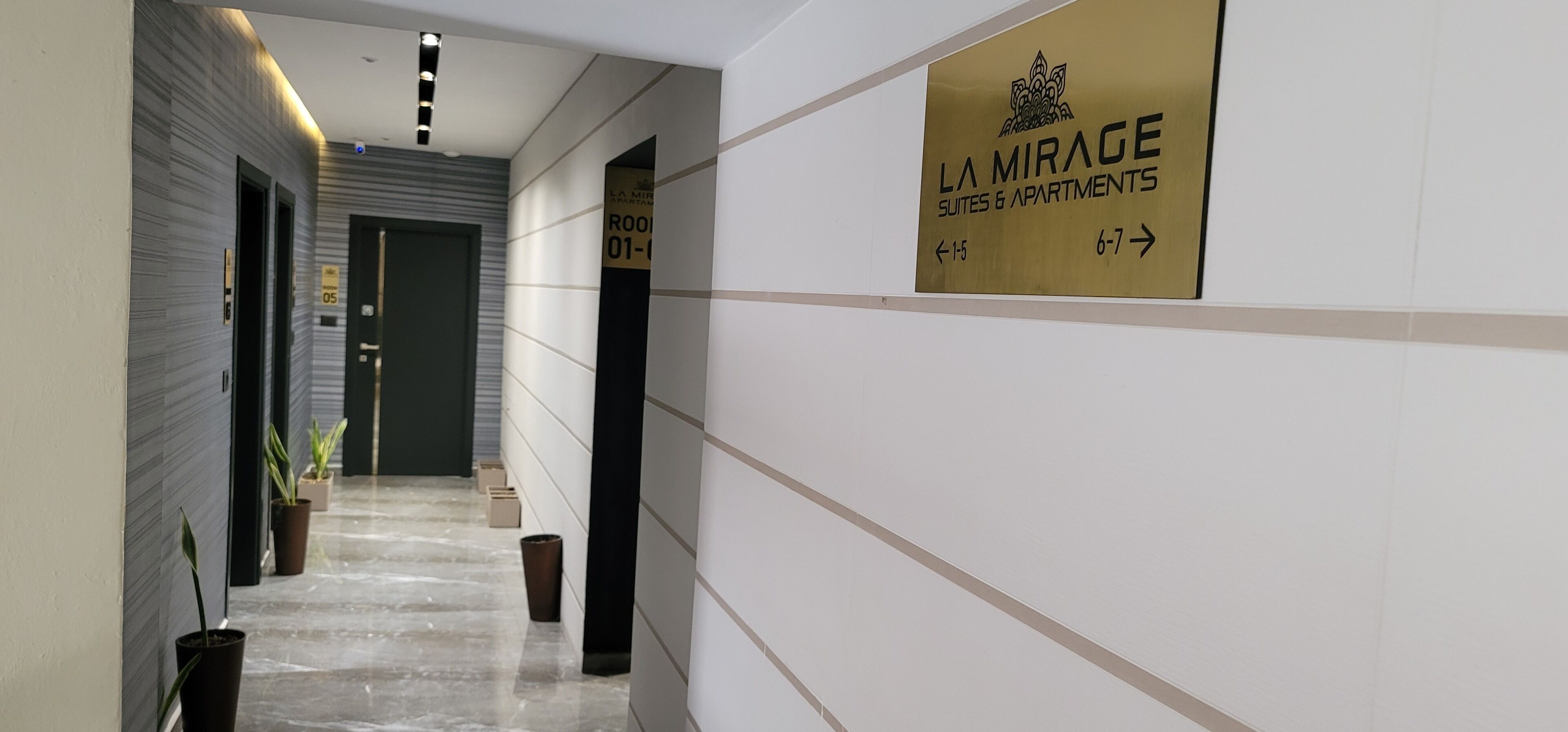 Een gang met een bordje 'La Mirage Suites & Apartments' waarop kamernummers 01-05 staan.